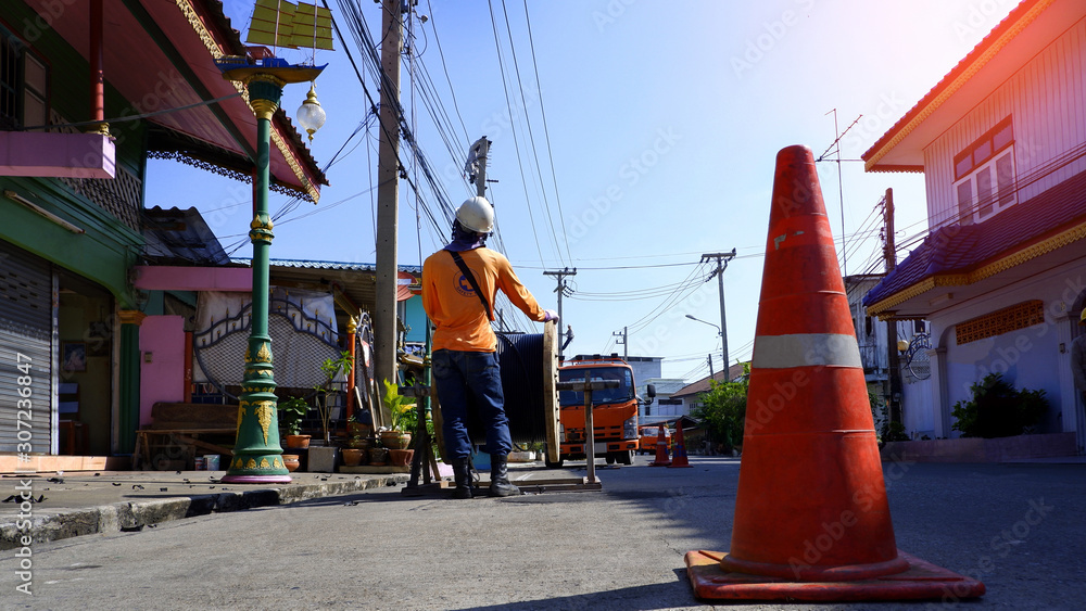 Fototapeta premium Low angle view of electricians team with crane truck are working to install electrical cable lines on electric power poles with flare light and blue sky background at morning time