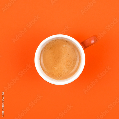 Fresh brewed coffee in ceramic cup over orange background.