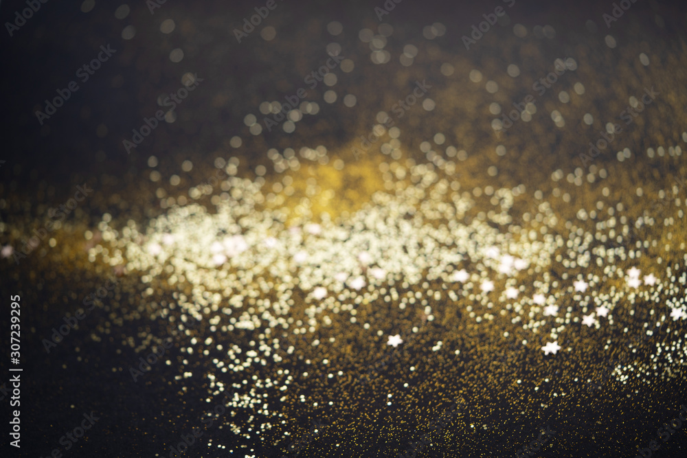 Beautiful Christmas light background. Abstract glitter bokeh and scattered sparkles in gold color, on black