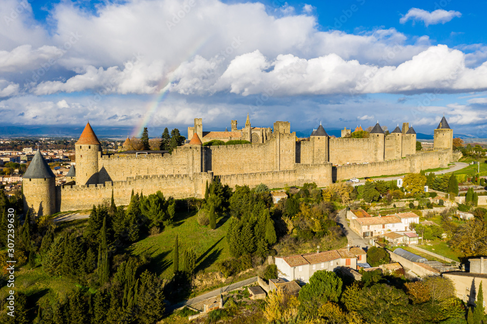 Rainbow over Cite de Carcassonne, a medieval hill-top citadel in the French city of Carcassonne, fortified by two castle walls. Aude, Occitanie, France. Aerial view. Pyrenees mountains background