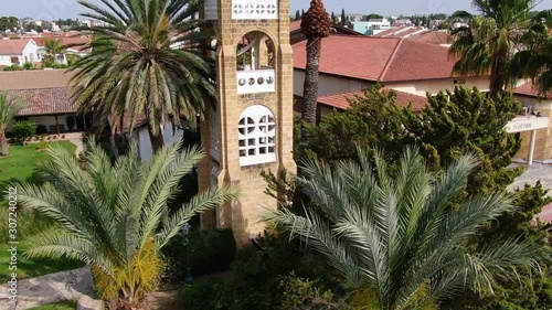 Rising shot of the Archaggelou Michael Church in Nicosia, Archaggelos Greece. Drone shot of the bell tower with palm trees in the daytime. photo