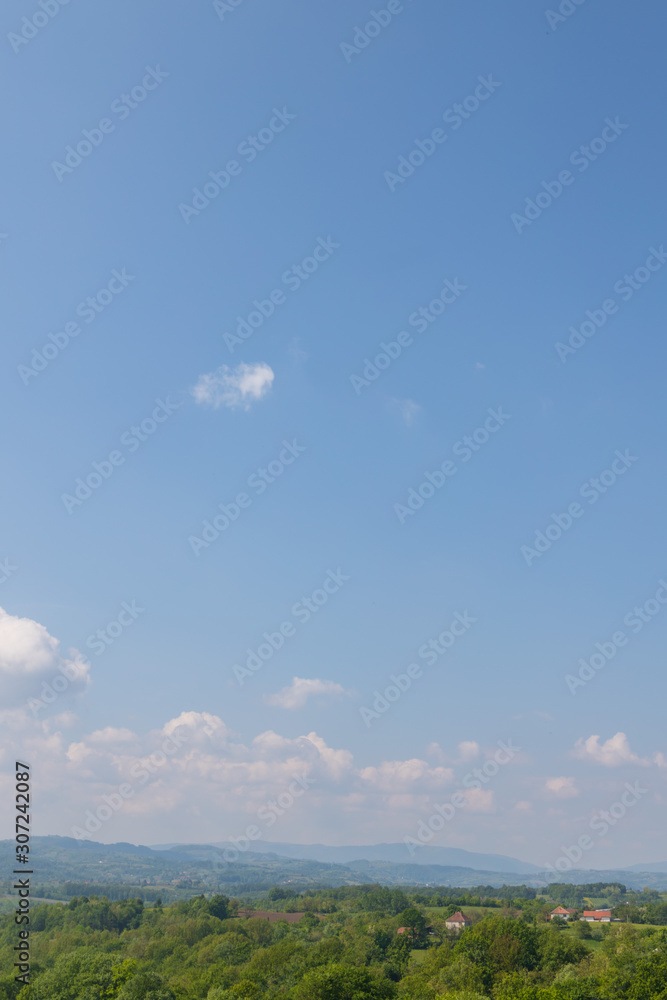 Obraz premium hilly landscape rich in tree vegetation with some houses and cloudy blue sky