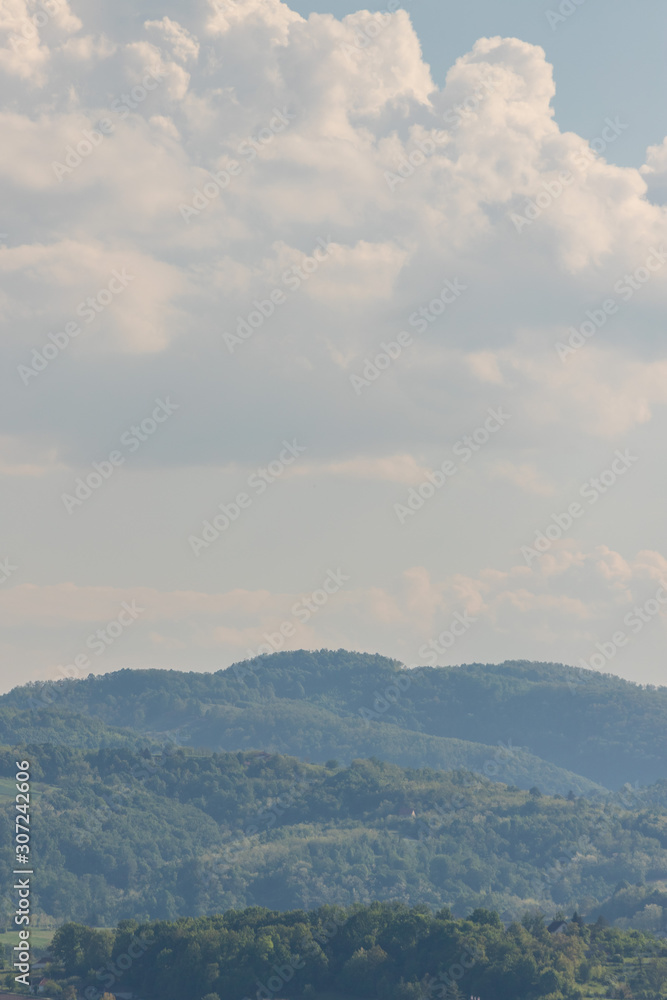 hilly landscape rich in tree vegetation with some houses and cloudy blue sky