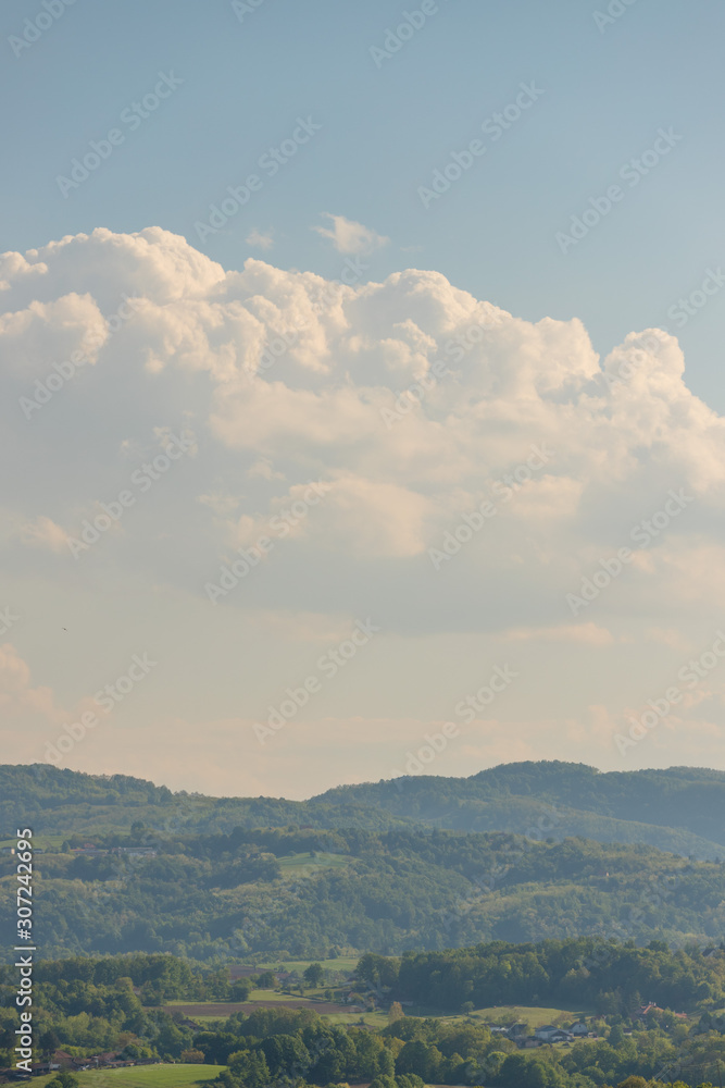 Fototapeta premium hilly landscape rich in tree vegetation with some houses and cloudy blue sky