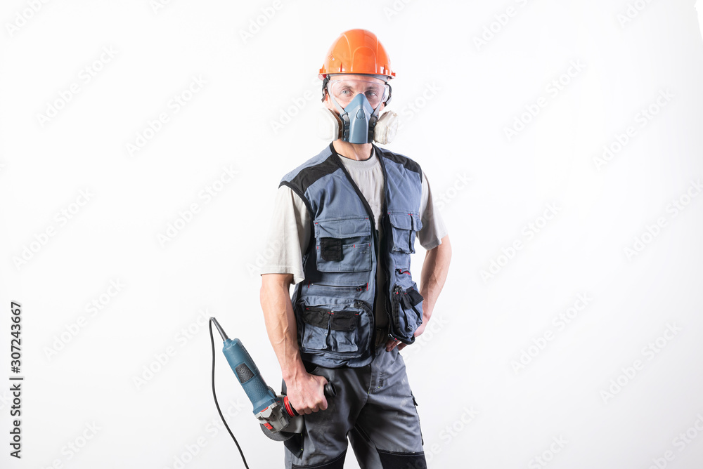 Naklejka premium Builder in a helmet and a respirator, with an angle grinder in his hands.