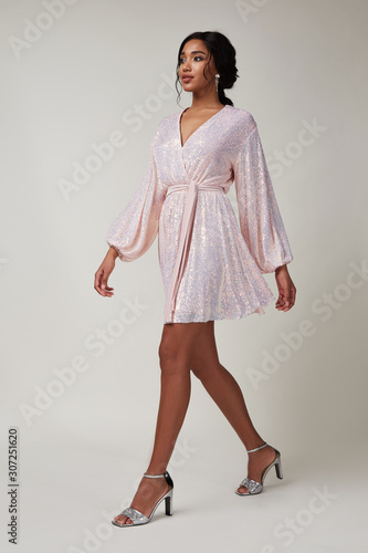 Beautiful sexy young woman brunette hair with evening make-up wearing a pink shine glitter dress high-heeled shoes party celebration clothes for meetings and walks date studio fun perfect body shape.