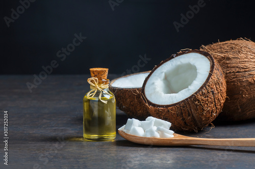 Glass bottle of coconut oil with fresh coconut fruit on rustic background, alternative theraphy medicine concept, Cocos nucifera