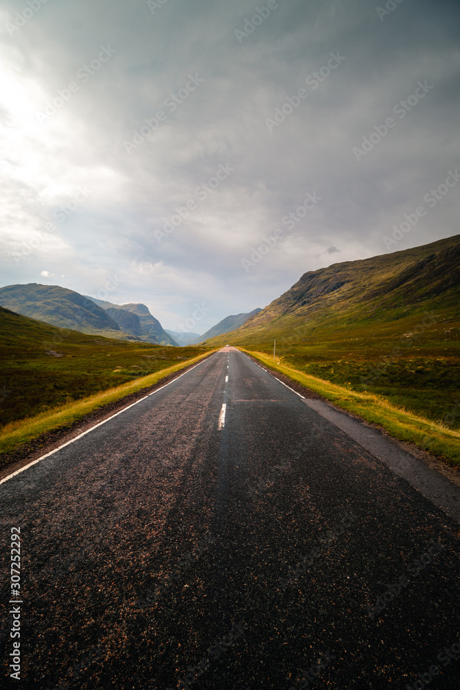 Naklejka premium A long Scotland asphalt road in the middle of nowhere, heading towards brighter future