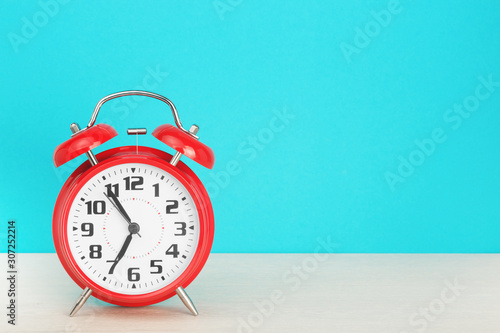 Red retro alarm clock with five minutes to seven o'clock, on wooden table on a blue background. The concept of time, holiday, 5 minutes to the event, deadline. Layout with copy space for your text.