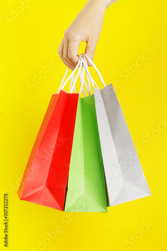 Hand holding colourful shopping or gift bag against yellow background. The concept of shopping or gifts.