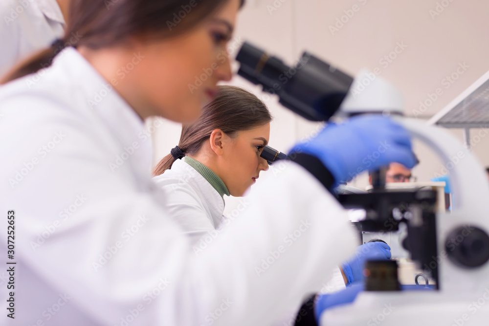 Two Young female scientist looking through a microscope in a laboratory doing research, microbiological analysis, medicine. Two Young female scientist looking through a microscope in a laboratory doing research, microbiological analysis, medicine.