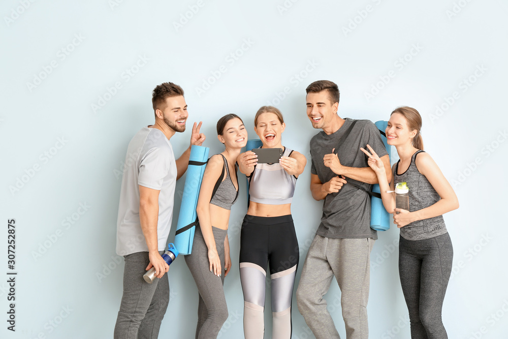 Group of people with yoga mats taking selfie near color wall