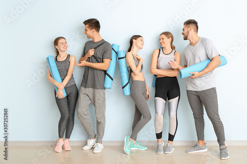 Group of people with yoga mats near color wall