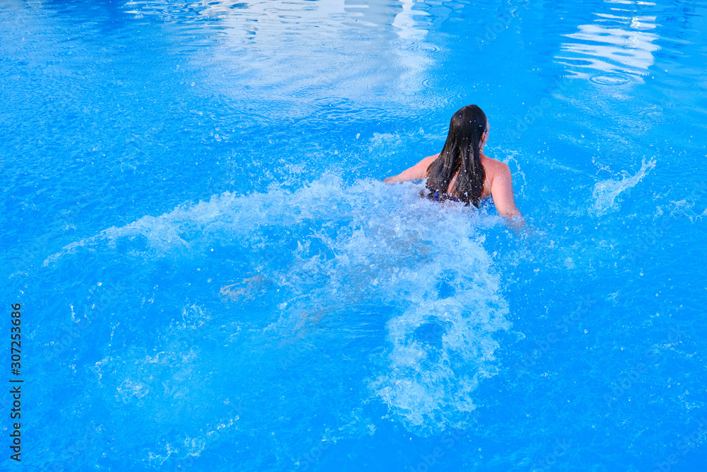 Girl swimming breaststroke in the pool, back view