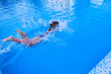 A woman jumps into the pool, entering the water and splashing