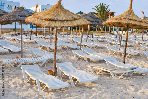 Empty sun loungers without people under straw umbrellas on the beach