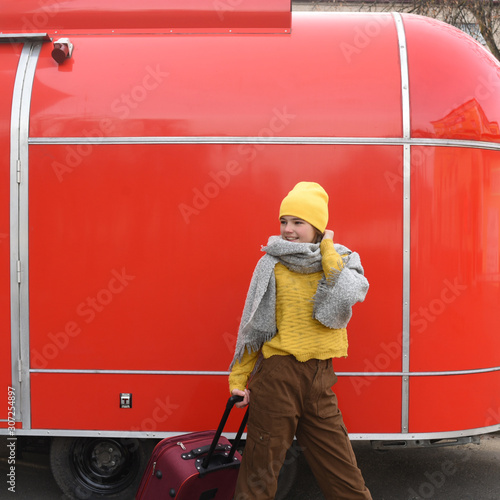 girl runs with a red suitcase on a red background. Large retro vintage van. Old car. Traveling in the winter. Girl in a yellow bright hat and knitted sweater. Travel concept.copy space