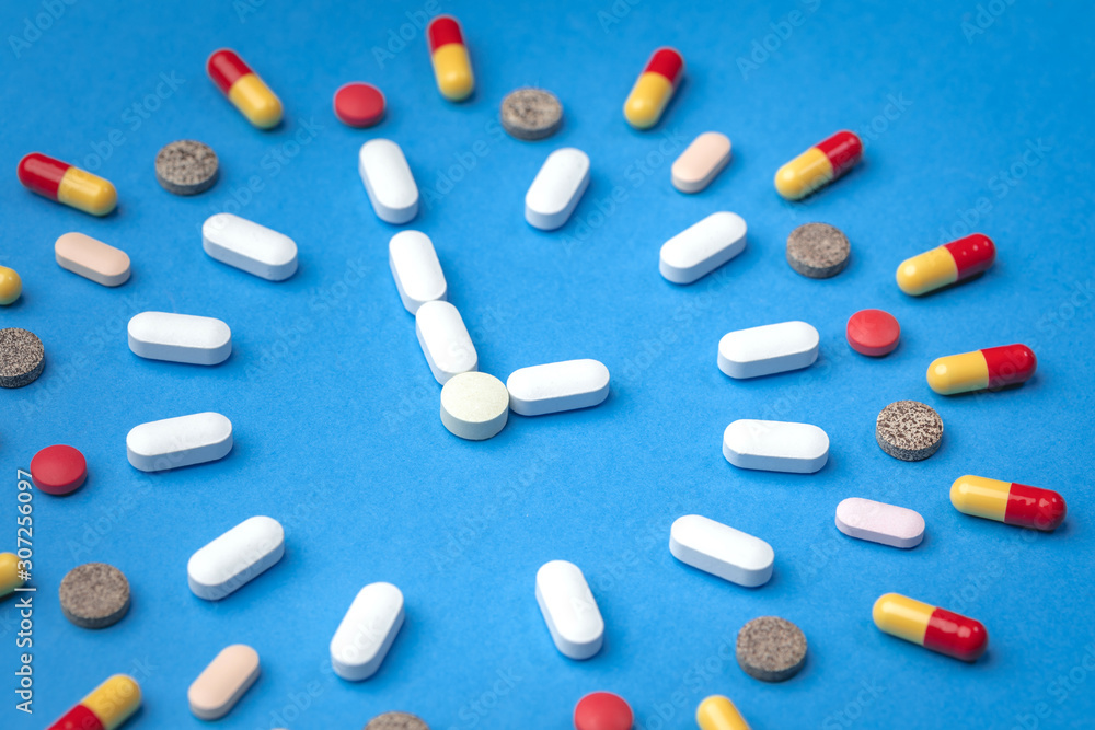Group of different pills arranged in form of clock on blue background. Time in pharmacy. Time in medicine. Group of different pills arranged in form of clock on blue background. Time in pharmacy. Time in medicine.