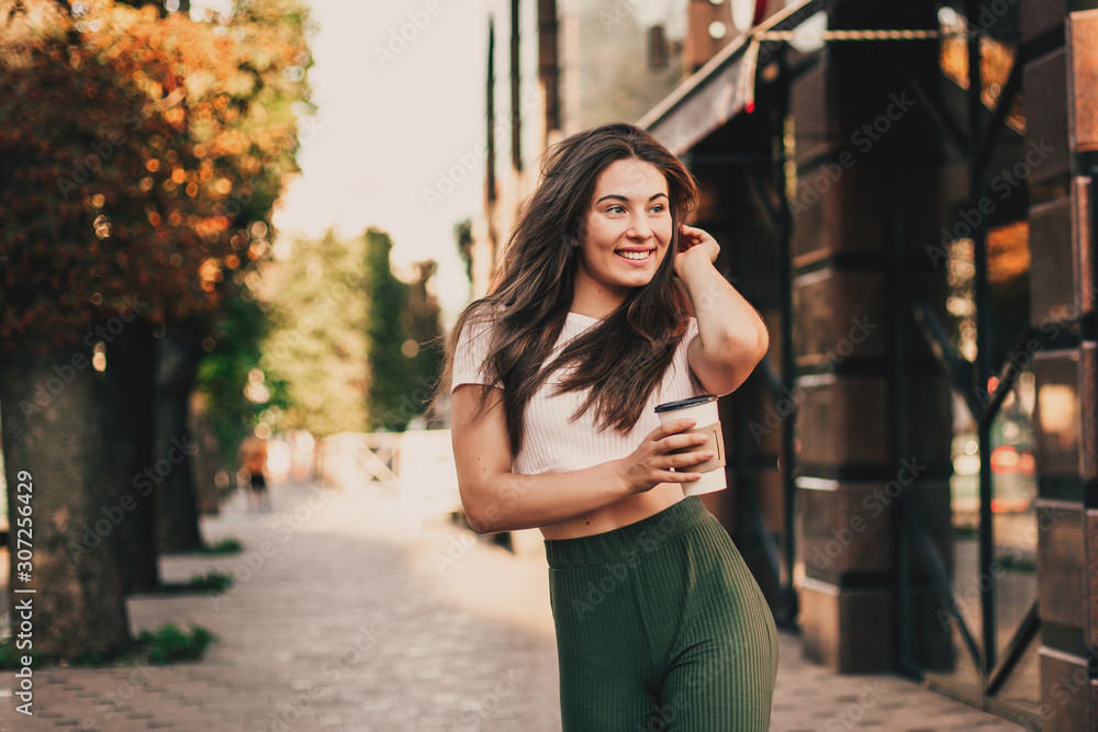 Smiling woman drink coffee walking on the city in summer day. Smiling woman drink coffee walking on the city in summer day.