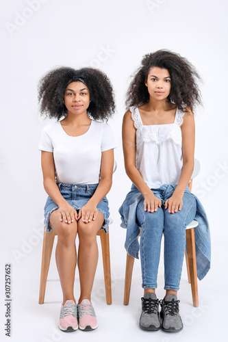 Portrait of young African-American women sitting on chairs against white background
