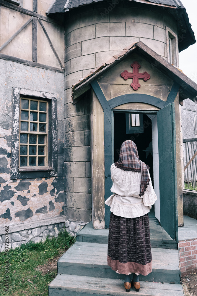 A woman stands praying at the door of an old catholic church