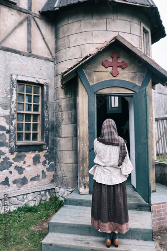 A woman stands praying at the door of an old catholic church