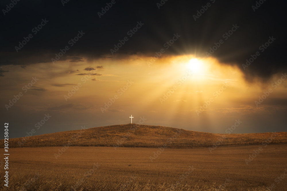 A sunrise over a white wooden religous cross on a brown hill in a deserted springtime landscape