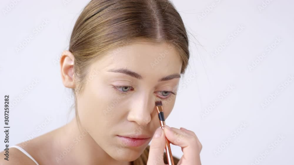Close up shot of beautiful woman using small makeup brush and putting on concealer around her eye Close up shot of beautiful woman using small makeup brush and putting on concealer around her eye
