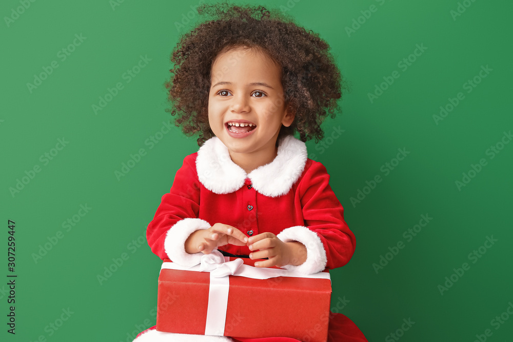 Little African-American girl in Santa costume and with gift on color background Little African-American girl in Santa costume and with gift on color background