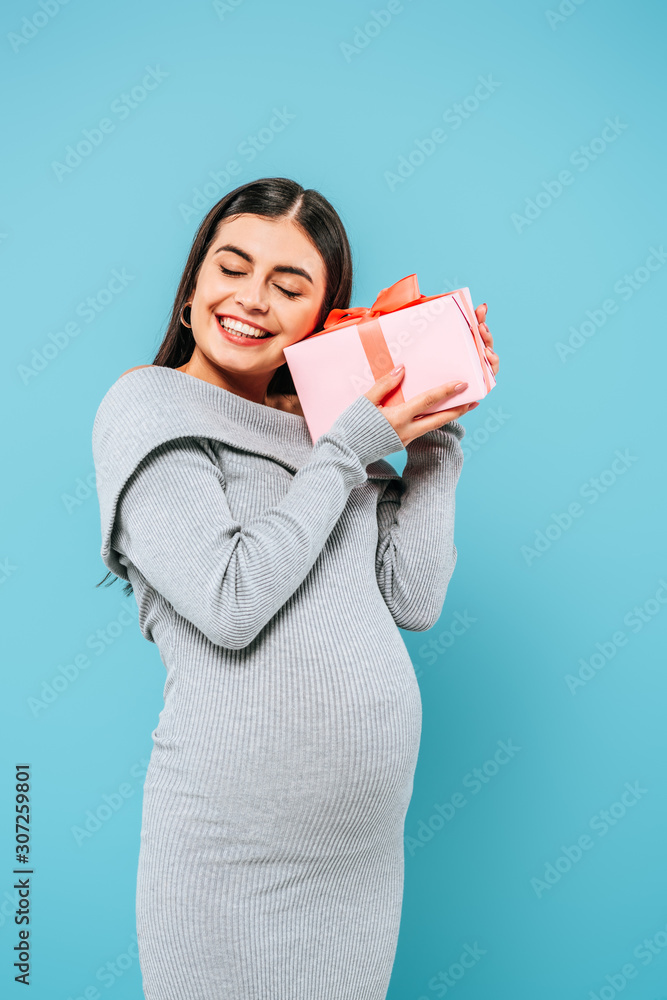smiling pregnant pretty girl holding present with closed eyes isolated on blue smiling pregnant pretty girl holding present with closed eyes isolated on blue