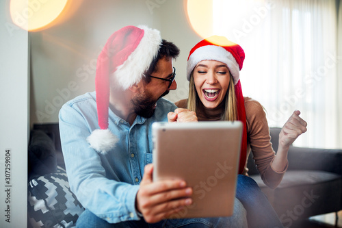  Love couple with Christmas hats on head using tablet and smiling
