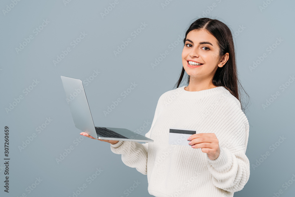 smiling pretty girl in white sweater holding laptop and credit card isolated on grey smiling pretty girl in white sweater holding laptop and credit card isolated on grey