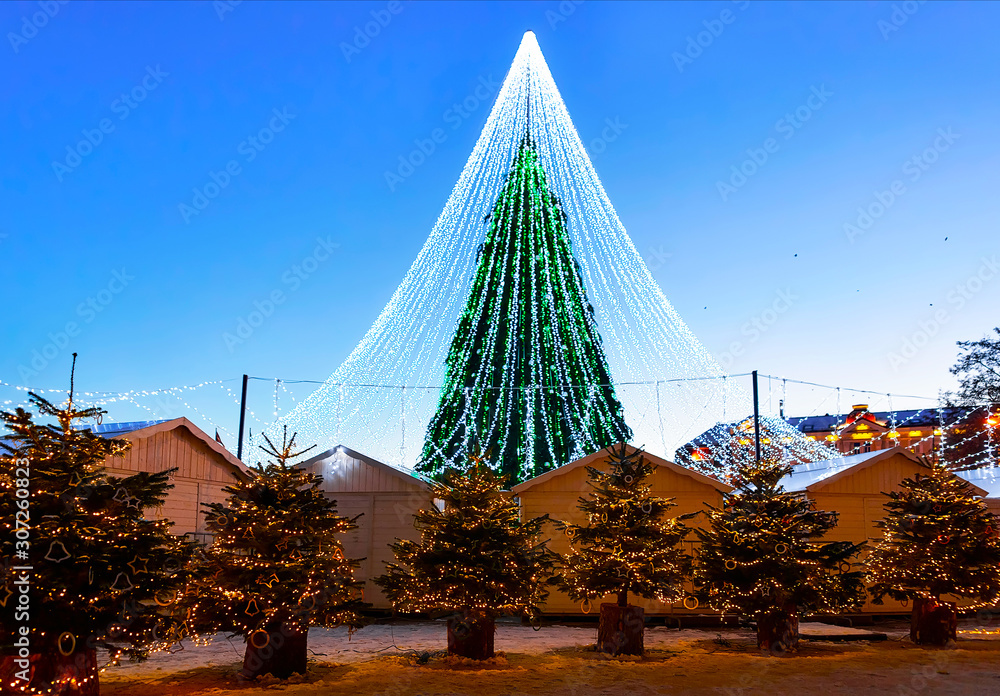 Fototapeta premium Night Cityscape with Christmas Market at Cathedral square in Winter Vilnius, Lithuania. Advent Fair Decoration and Stalls with Crafts Items on the Bazaar. Lithuanian street Xmas and holiday