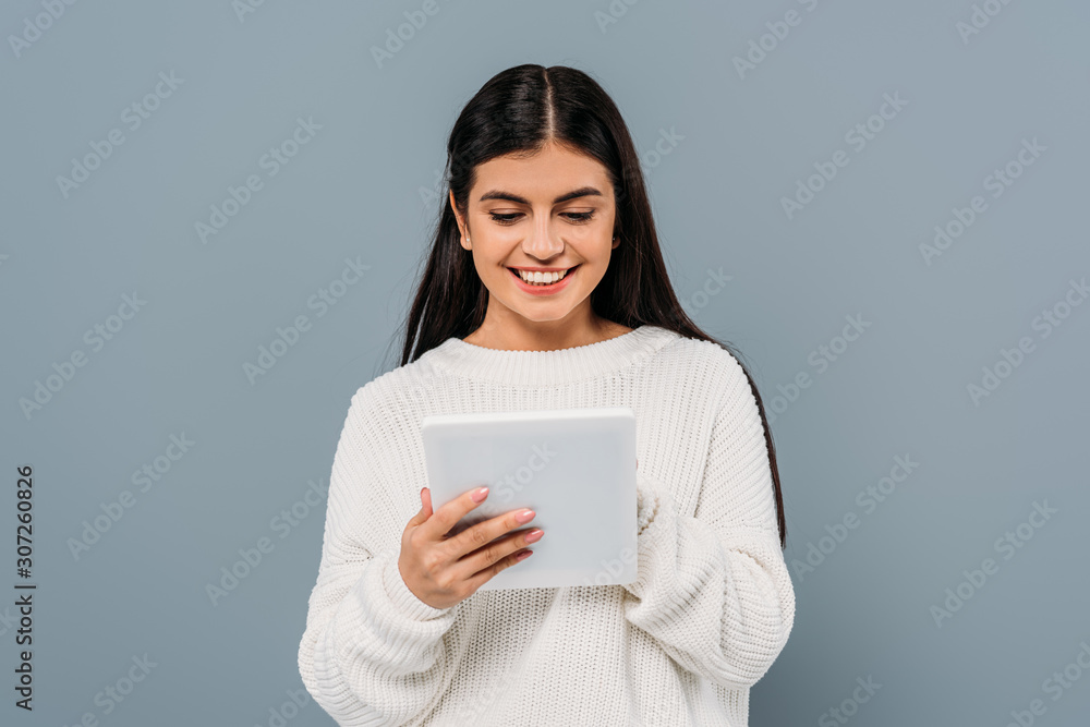 smiling pretty brunette girl in white sweater using digital tablet isolated on grey smiling pretty brunette girl in white sweater using digital tablet isolated on grey