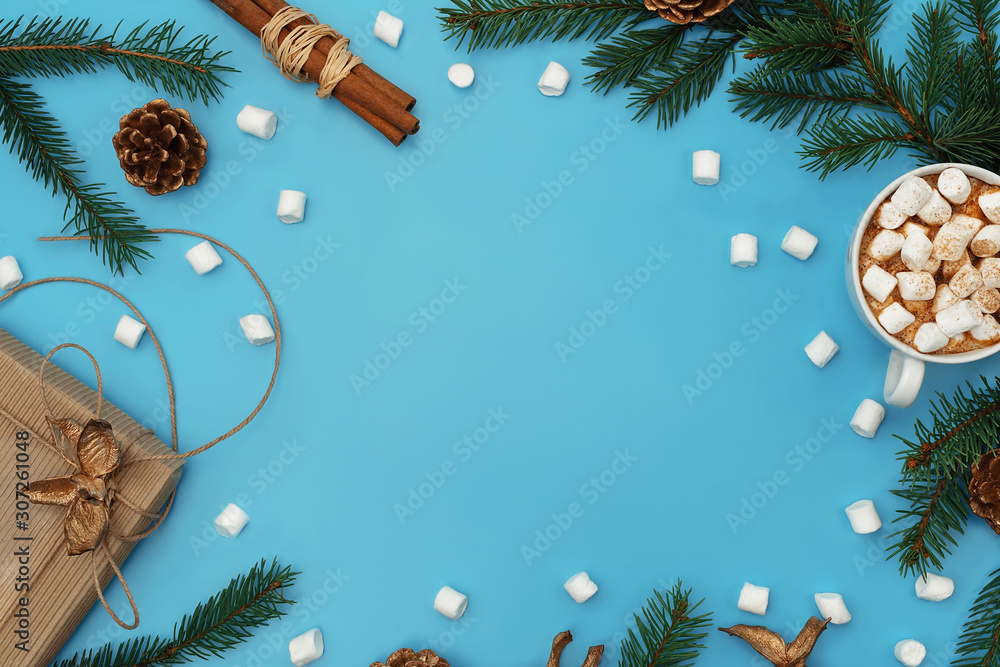 Trendy Christmas background of hot chocolate with marshmallow, ginger cookies, craft gift box, Christmas tree branches with golden cones on cyan blue backdrop. Holiday season concept. Copy space. Flat