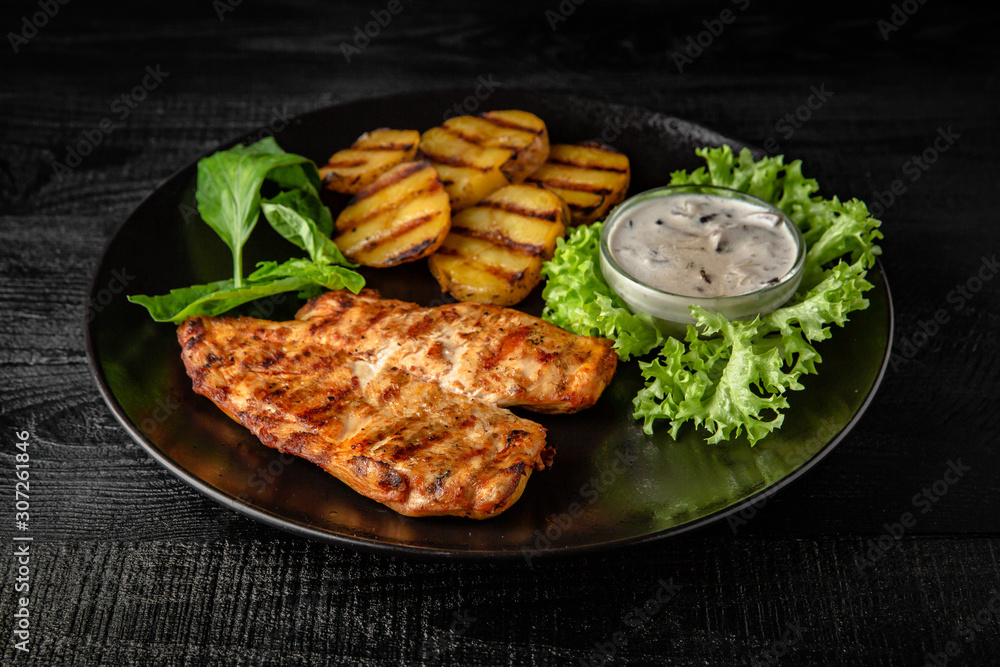 Grilled chicken fillet with homemade potatoes and sauce. Black boards background Grilled chicken fillet with homemade potatoes and sauce. Black boards background