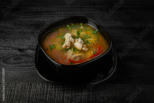 Chicken soup on a broth with pieces of meat, noodles and herbs. On a black background