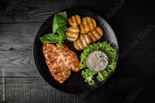 Grilled chicken fillet with homemade potatoes and sauce. Black boards background