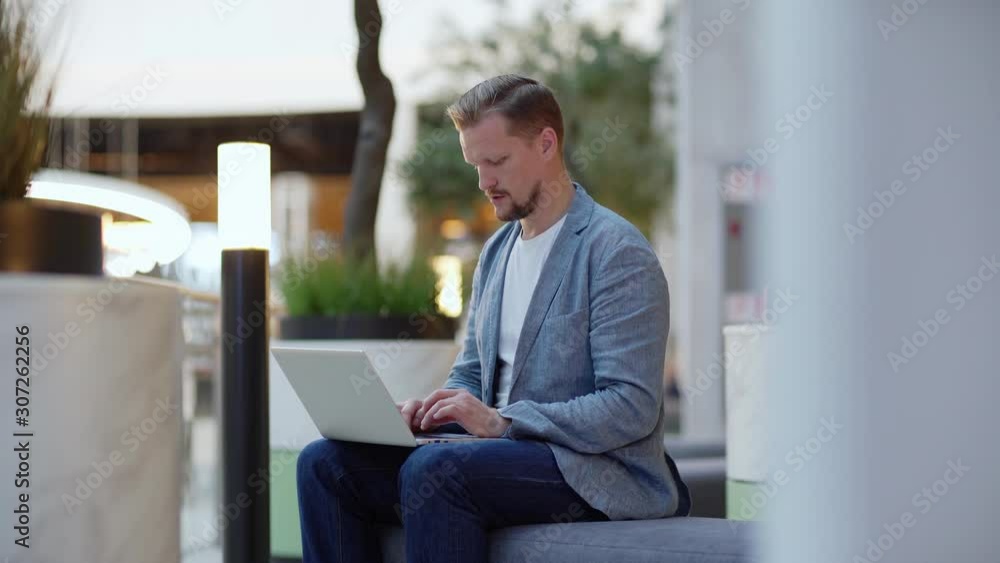 Tracking medium shot side view of middle aged businessman sitting on sofa in office lobby and typing on laptop computer Tracking medium shot side view of middle aged businessman sitting on sofa in office lobby and typing on laptop computer