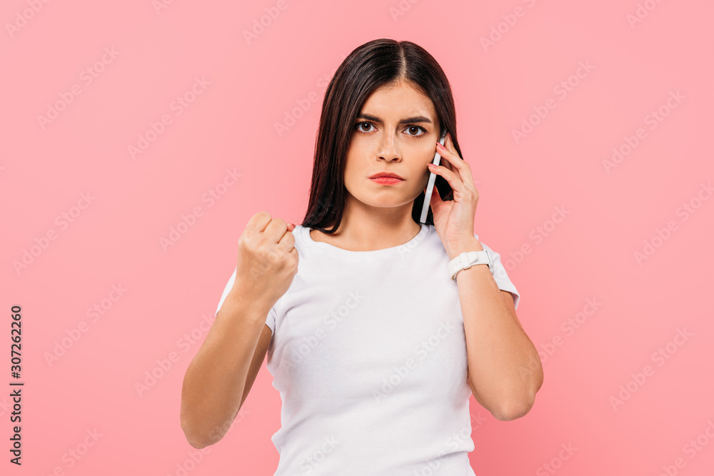 angry pretty brunette girl talking on smartphone and showing fist isolated on pink angry pretty brunette girl talking on smartphone and showing fist isolated on pink