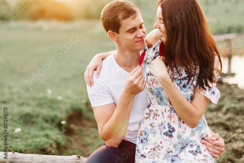Young loving couple hugging near lake with red paper heart in hand.