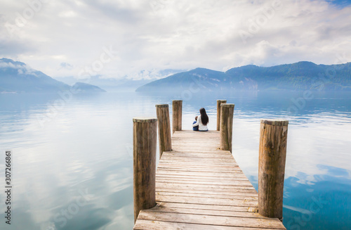 A mother and little boy sit on a wooden pier beside Lake Lucerne on the background of snowcapped mountains in Weggis, Switzerland. Concept of vacation, relaxation, family, quality time. 