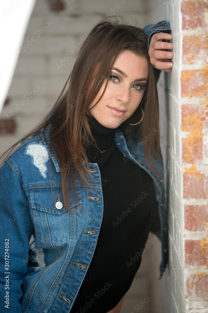 Stunning young brunette woman wearing denim jacket, black turtleneck fashion headset leaning against brick wall