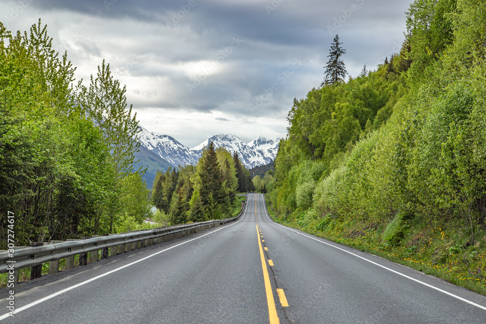 Scenic road with storm clouds and snow covered mountains in Alaska
