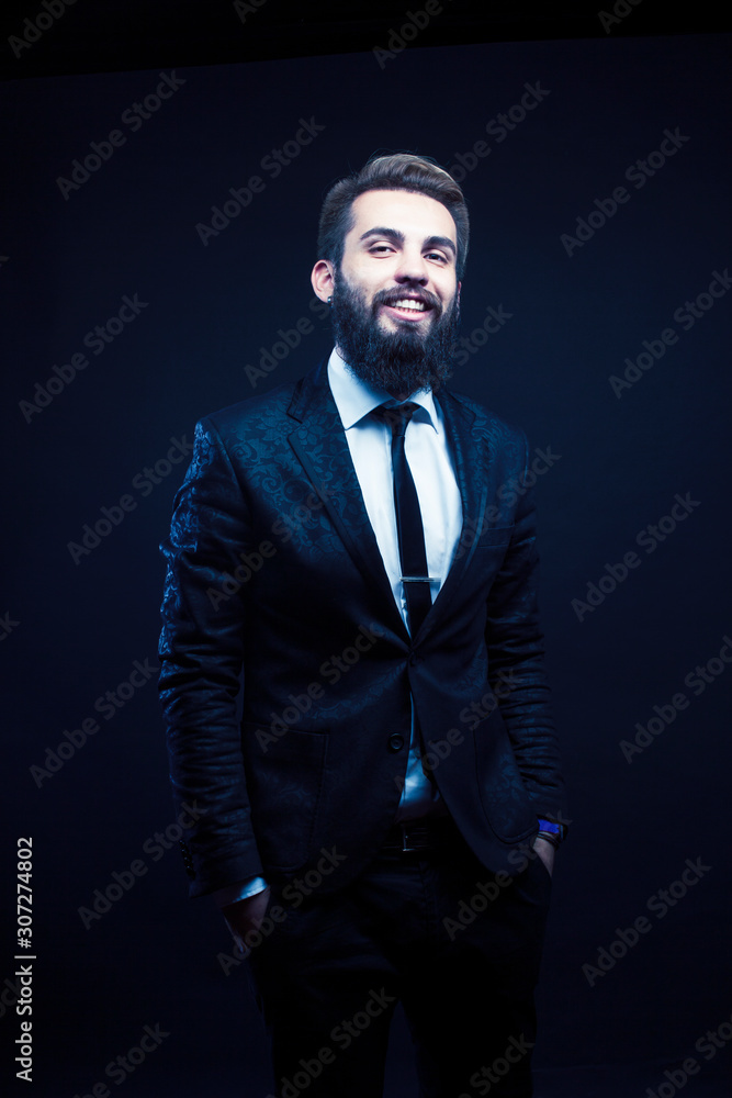 young pretty modern hipster business man with beard standing on black background, fashion style hairstyle