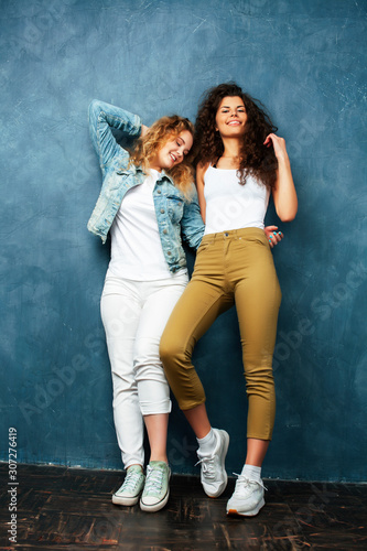 young pretty teenage girls friends with blond and brunette curly hair posing cheerful on blue background, lifestyle people concept © iordani