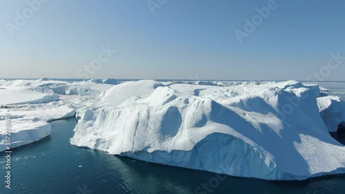 Aerial drone view of banks of ice in the area of Ilulissat, Greenland, flying closely over the hills of arctic white and turquoise ice, floating in the Baffin sea with a clear, calm weather