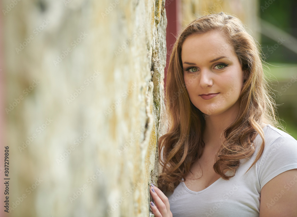 Stunning young blonde woman poses near an old stone wall head shot