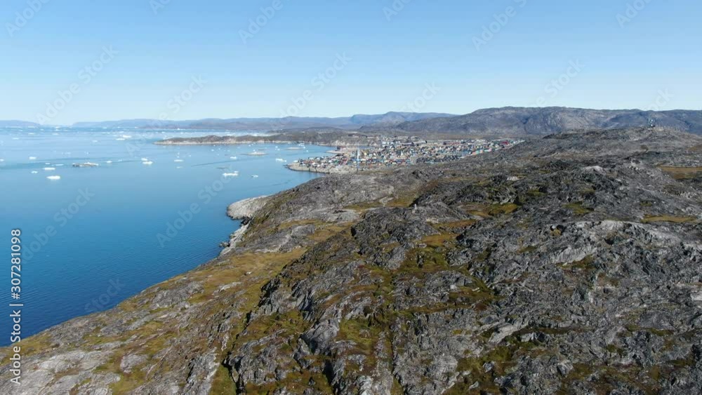 Slow drone aerial ride over the rocky terrain of Ilulissat, Greenland, revealing the high detailed surface of this natural scenery, with the harbor and the little town in the background and icebergs Slow drone aerial ride over the rocky terrain of Ilulissat, Greenland, revealing the high detailed surface of this natural scenery, with the harbor and the little town in the background and icebergs