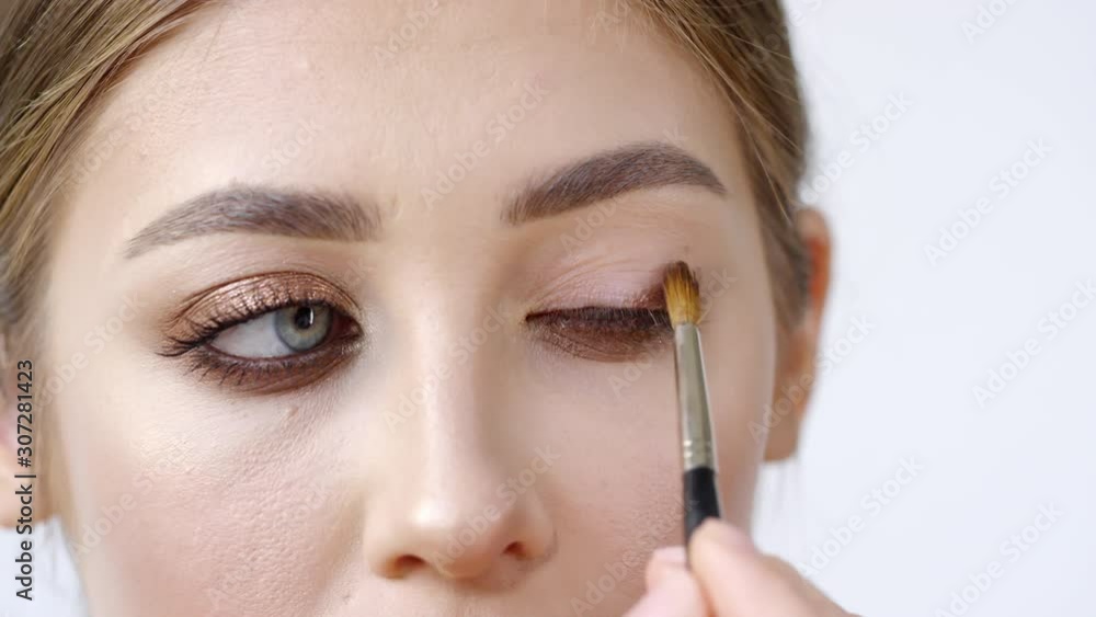 Extreme close up shot of young woman putting metallic eyeshadow on eyelid using makeup brush Extreme close up shot of young woman putting metallic eyeshadow on eyelid using makeup brush